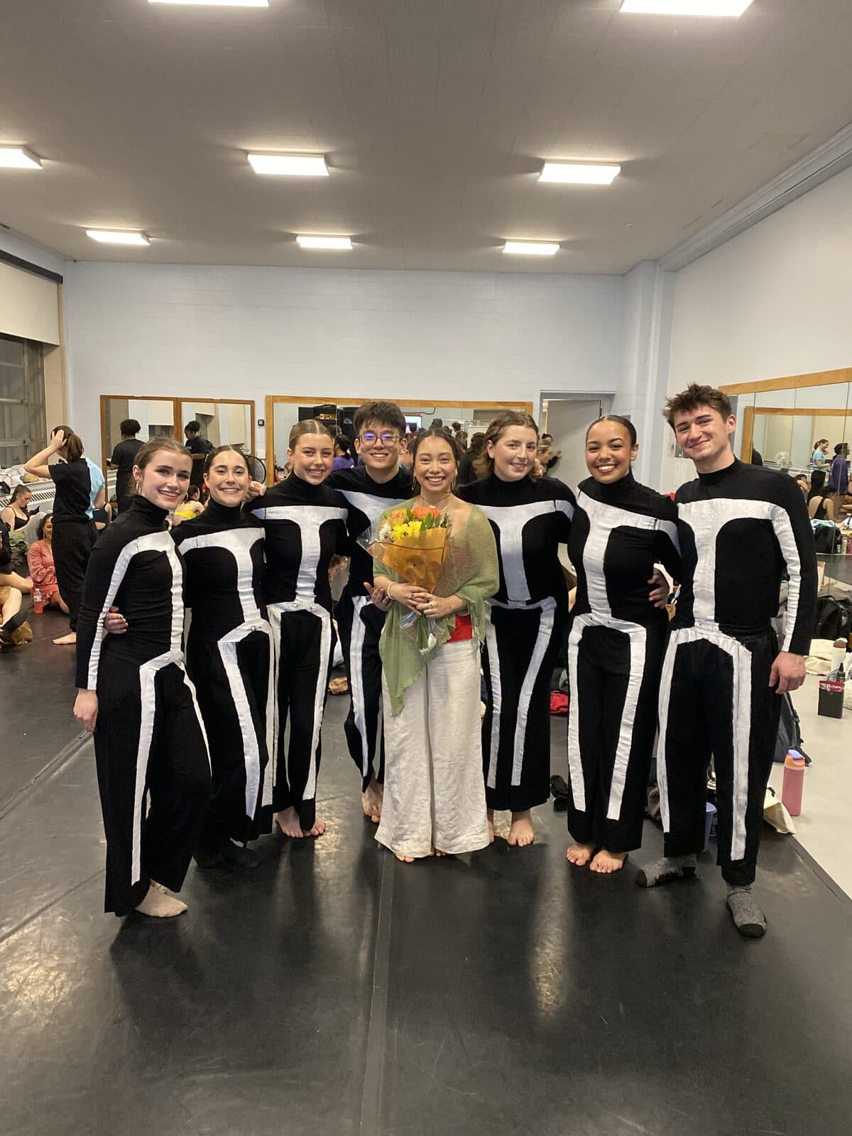 The cast of Not Yet Perfect in black costumes striped with white stick-figure lines, posing together in a rehearsal studio.